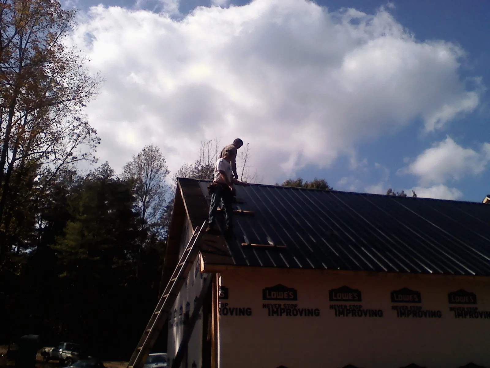 Roofer fastening dark metal panels high against a cloudy sky, from a Roof Inspection job in Jackson